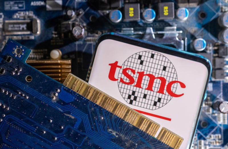 The photo illustration displays the smartphone with the TSMC (Taiwan Semiconductor Manufacturing Company) logo and a computer motherboard.