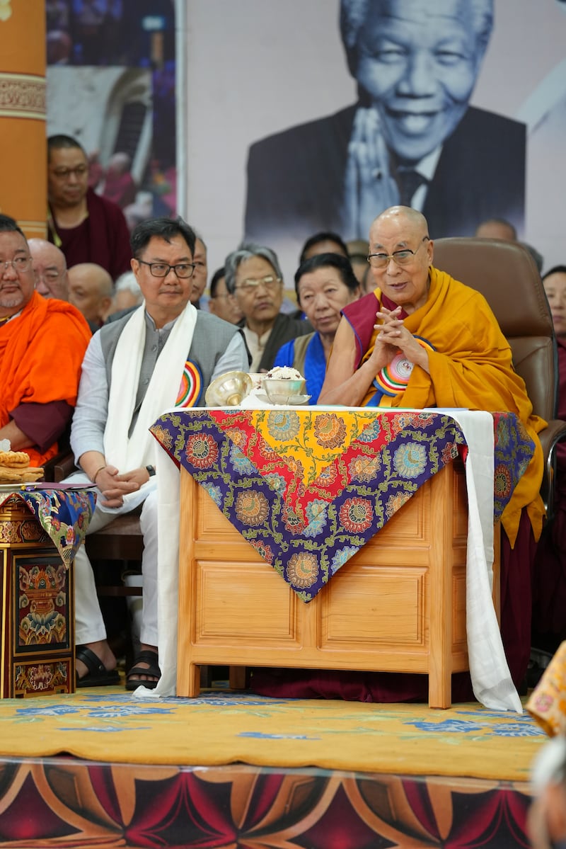 Tibetan spiritual leader the Dalai Lama is seated beneath an image of Nelson Mandela during celebrations on the 90th birthday of the Dalai Lama at the Main Temple in Dharamsala, India, July 6, 2025. At left is Kiren Rijiju, Indian Minister of Parliamentary Affairs and Minister of Minority Affairs.